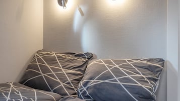 Ein Raumeck mit einer strukturierten Wand und einer Leuchte. Auf einem Sofa liegen zwei Kissen mit einem geometrischen Muster.