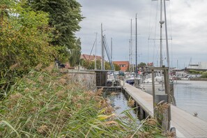 Un puerto deportivo con barcos amarrados, un muelle que se adentra en el agua y un edificio con techo rojo al fondo.