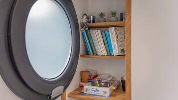 Een kamer met een rond raam, een boekenkast met boeken en decoratieve objecten, en een kleine tafel met een spel.