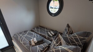 A compact room with a bed, a small window, and a wooden ceiling structure.