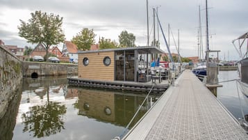 Ein schmaler Wasserweg mit einem hölzernen Steg, der zu einem kleinen Gebäude mit großen Fenstern führt.