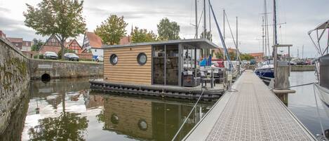 Un étroit canal, bordé d’un quai en bois qui mène à un petit bâtiment doté de grandes fenêtres.