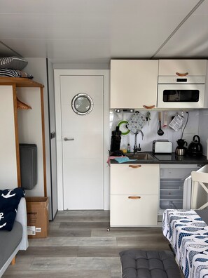 Una cocina compacta con armarios blancos, microondas y diferentes utensilios de cocina.
