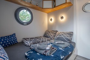 Habitación pequeña con cama, almohadas, ventana y lámpara fijada a la pared.