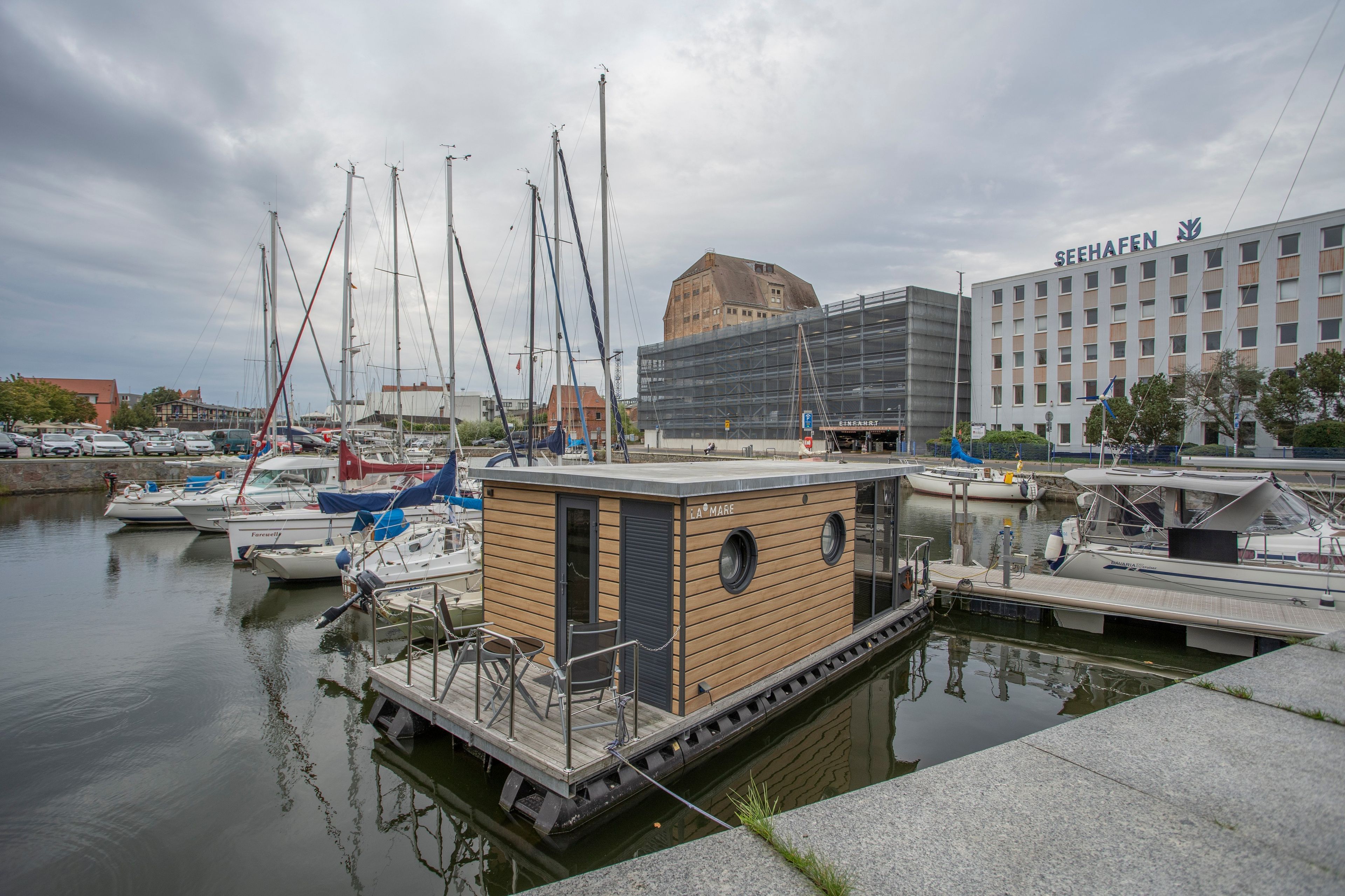 En havn med fortøjede både, en lille træbygning og et hus med skiltet 'SEEHAFFEN'.