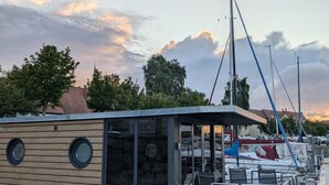 A floating structure with a wooden exterior, a glass door, and a small deck with chairs and tables.