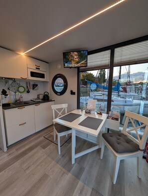 Une cuisine moderne avec des meubles blancs, un four encastré et un coin repas comprenant une table et des chaises blanches.