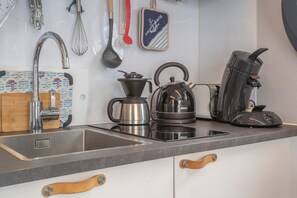 Una cocina con un lavamanos, un hervidor, una cafetera y varios utensilios.