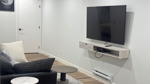Un salon moderne avec un canapé noir, une table basse ronde et un téléviseur à écran plat fixé au mur.