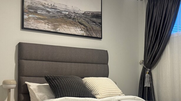 Une chambre à coucher avec une tête de lit rembourrée de couleur grise, une couvre-lit blanche et deux oreillers.