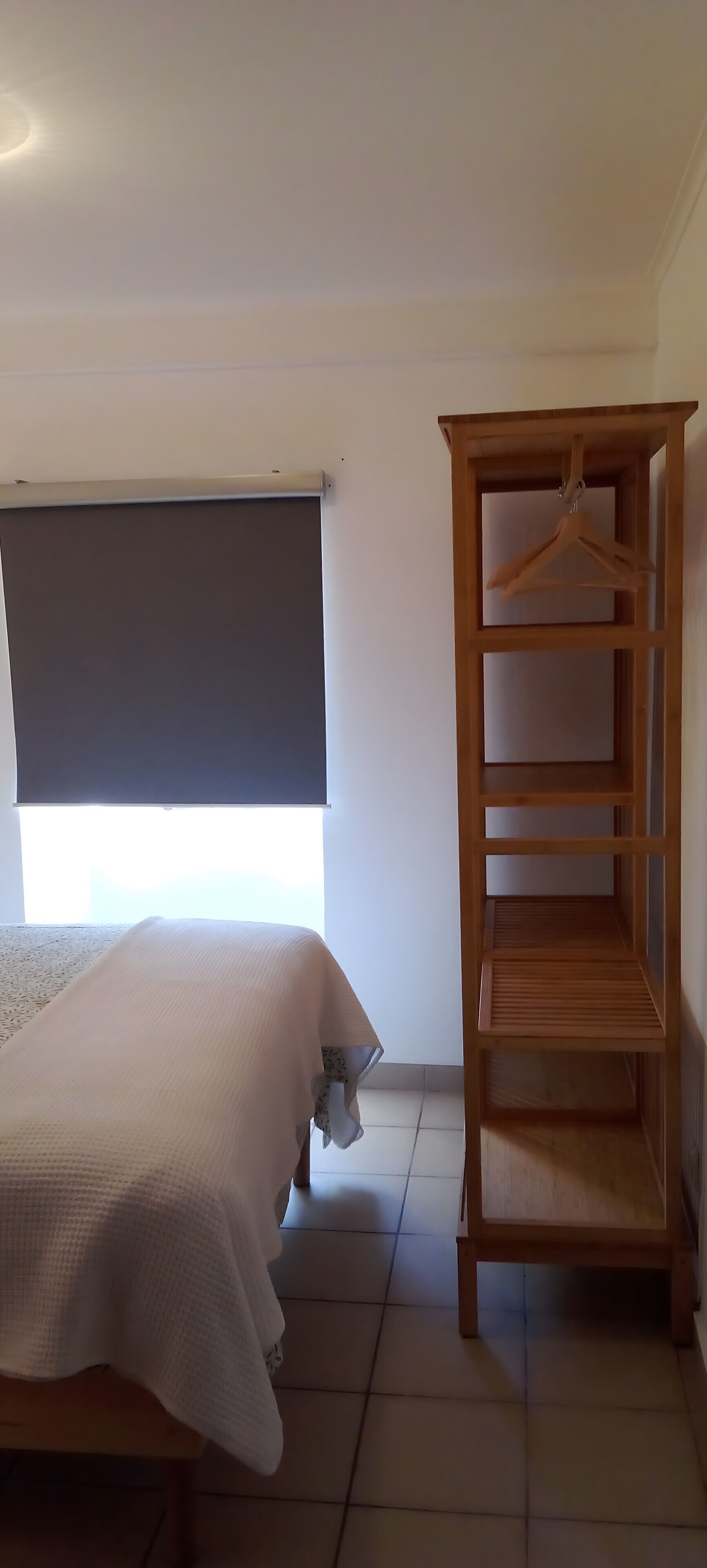Une chambre à coucher avec un lit, une armoire en bois, une fenêtre avec un store et un sol carrelé.