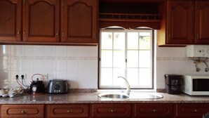 A kitchen with wooden cabinets, a white tiled backsplash, a sink, a toaster, a kettle, and a microwave. - Refuge - "Vivenda Chã" (Ribeira Funda)