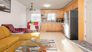 Eine moderne Küche mit Holzausstattung, einem Edelstahlkühlschrank und einem Essbereich mit gelbem Sofa und Glastisch.