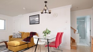 Ein modernes Wohnzimmer mit einem gelben Sofa, einem Glastisch, roten Sesseln, einer Topfpflanze und einer Chandelüster.