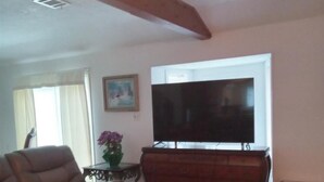A living room with a brown leather sofa, a glass coffee table, a TV on a wooden stand, and a painting on the wall. - 3-bedroom house in peaceful Magnolia with cool AC on 7.5 acres. (Magnolia)