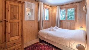 A wooden-paneled bedroom with a bed, curtains, and a window. - Chalet du Grand Air - Welkeys (Megève)