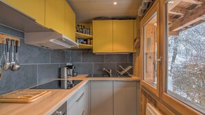 A modern kitchen with wooden cabinets, a stainless steel sink, and a window overlooking a snowy landscape. - Chalet du Grand Air - Welkeys (Megève)
