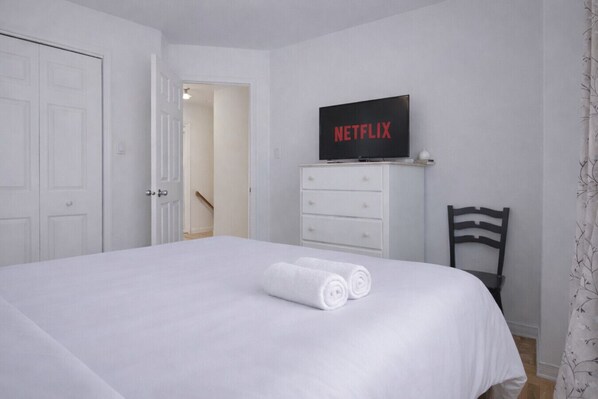 A hotel room with a bed, a TV on a dresser, a chair, and a door.