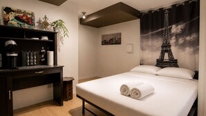Une chambre d’hôtel avec un lit, un bureau doté d’une machine à café, une plante et un tableau représentant la Tour Eiffel.