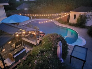 Een achtertuin met een zwembad, lichtjes, tuinmeubilair en een barbecue.