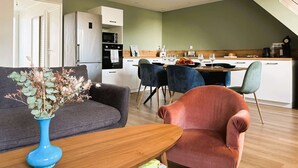 Un moderno salón con un sofá, una mesa de centro y un florero. Cuenta con una zona de cocina con una mesa de comedor y sillas.