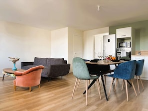 A modern living room with a grey sofa, a pink armchair, and teal chairs. A dining table with a vase of dried flowers is in the center. - Kalonn Ar Mor, beautiful 3-star 4-room apartment at the foot of the bay! (LA FORET FOUESNANT)