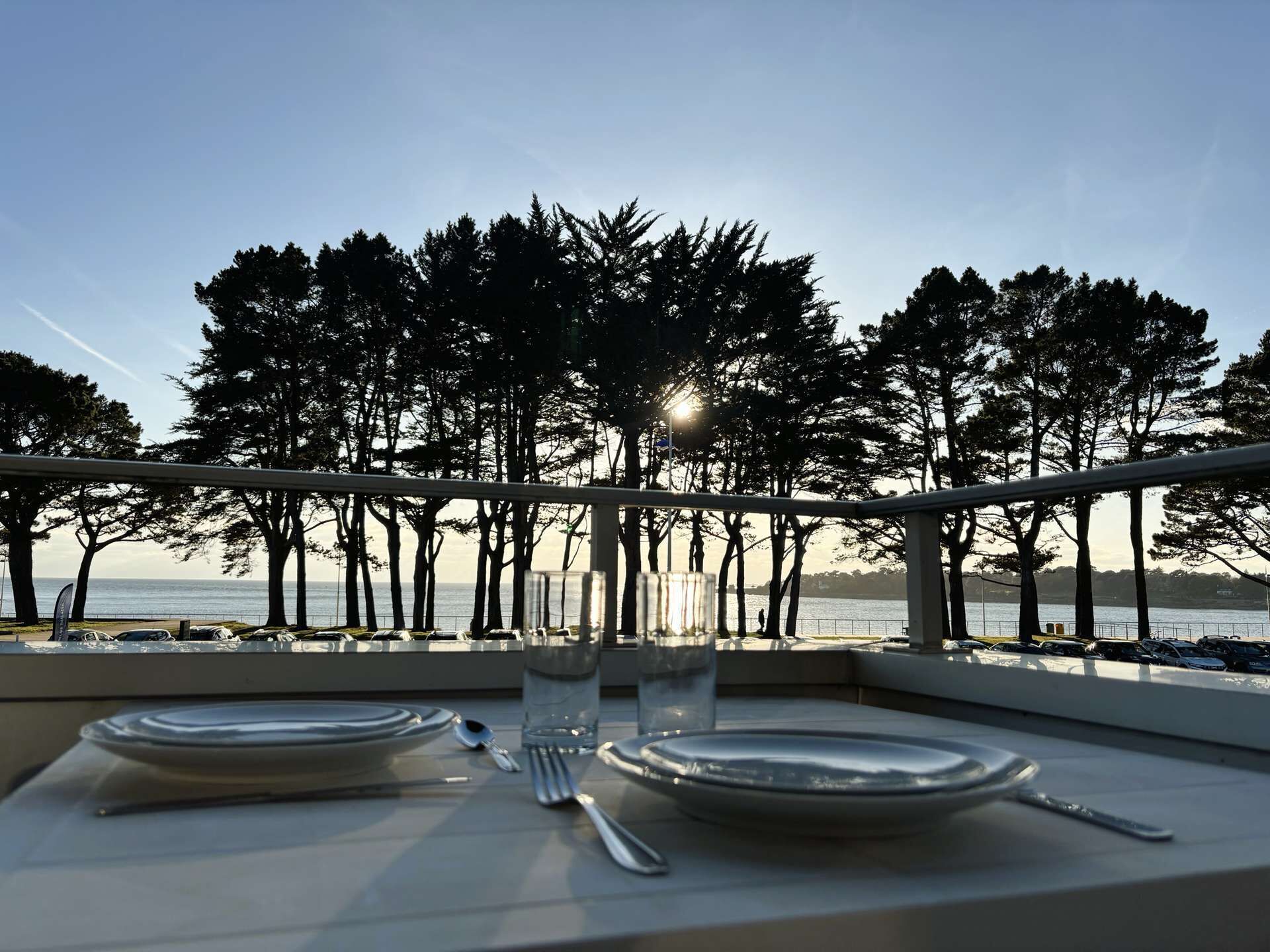 A table set for two with a view of the sea and trees.