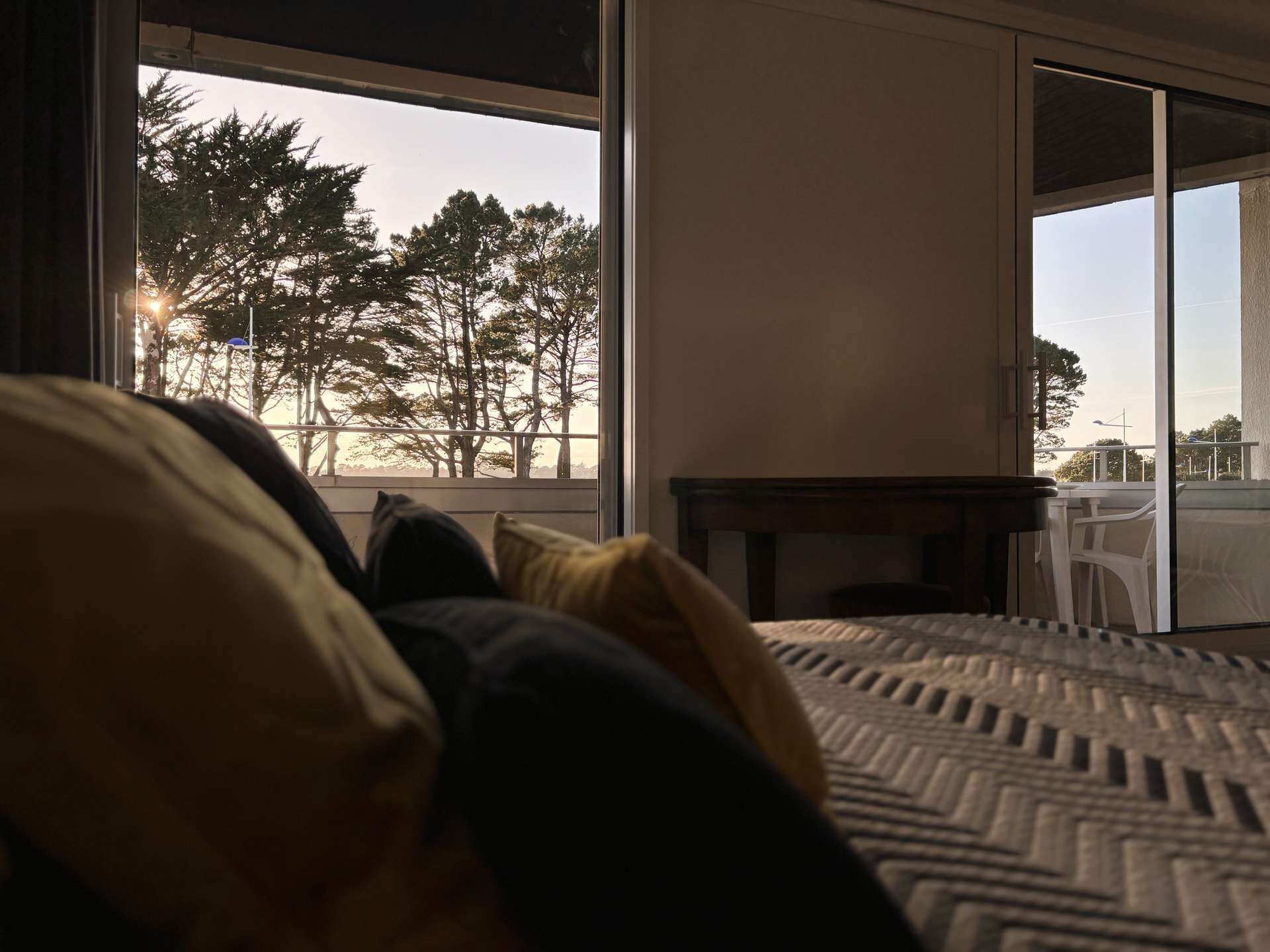 Een slaapkamer met een groot bed, uitzicht op bomen en een balkon door een schuifdeur.
