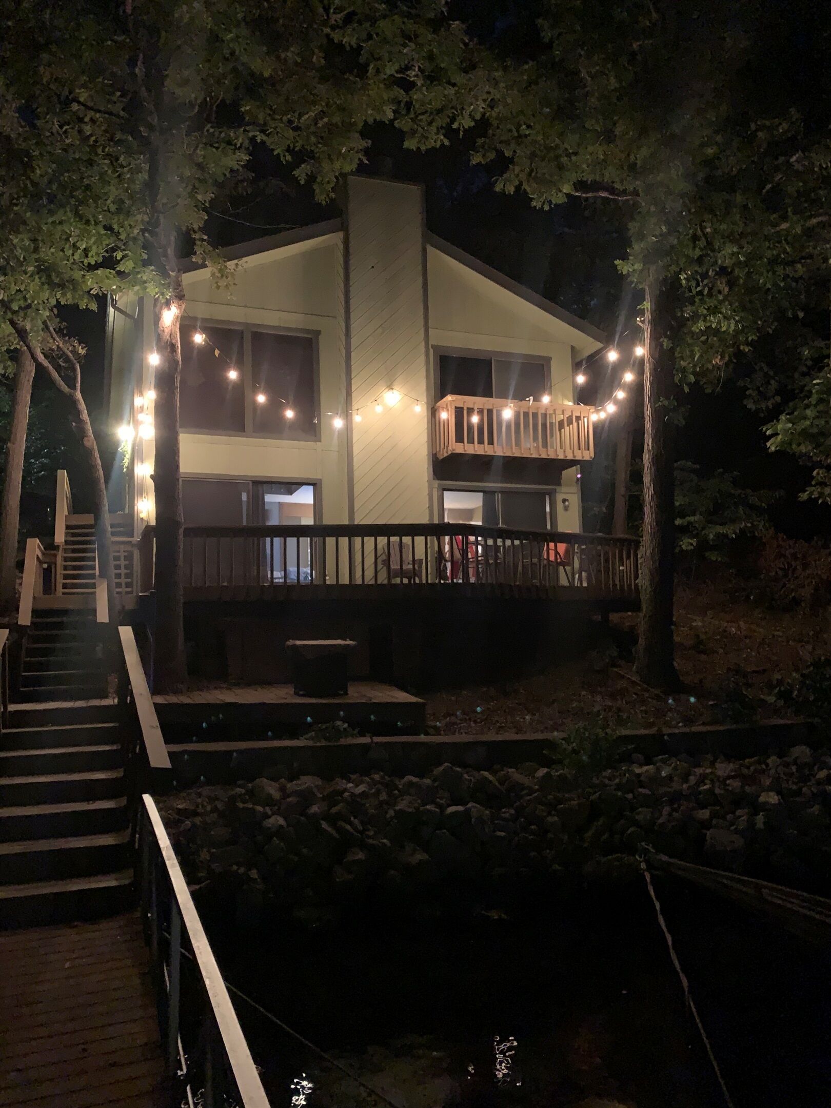 Een modern gebouw met een houten terras, lichtjes en een trap naar een hoger gelegen niveau.