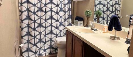 Um banheiro com cortina de chuveiro estampada, vaso sanitário, pia com espelho e um pequeno armário com produtos de higiene.