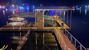 A dock with a covered seating area, a boat, and a calm water body reflecting lights. - Sunset lake retreat: kayaks & NEW: boat rental! (Lake Ozark)