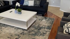 Una sala de estar con un sofá negro, una mesa de centro blanca y una alfombra estampada.