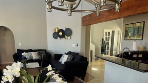 Un comedor con una mesa larga dispuesta para seis personas, una araña y una cocina moderna al fondo.