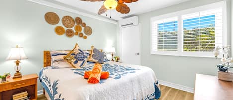 A bedroom with a bed, a ceiling fan, a window with blinds, and decorative wall art.