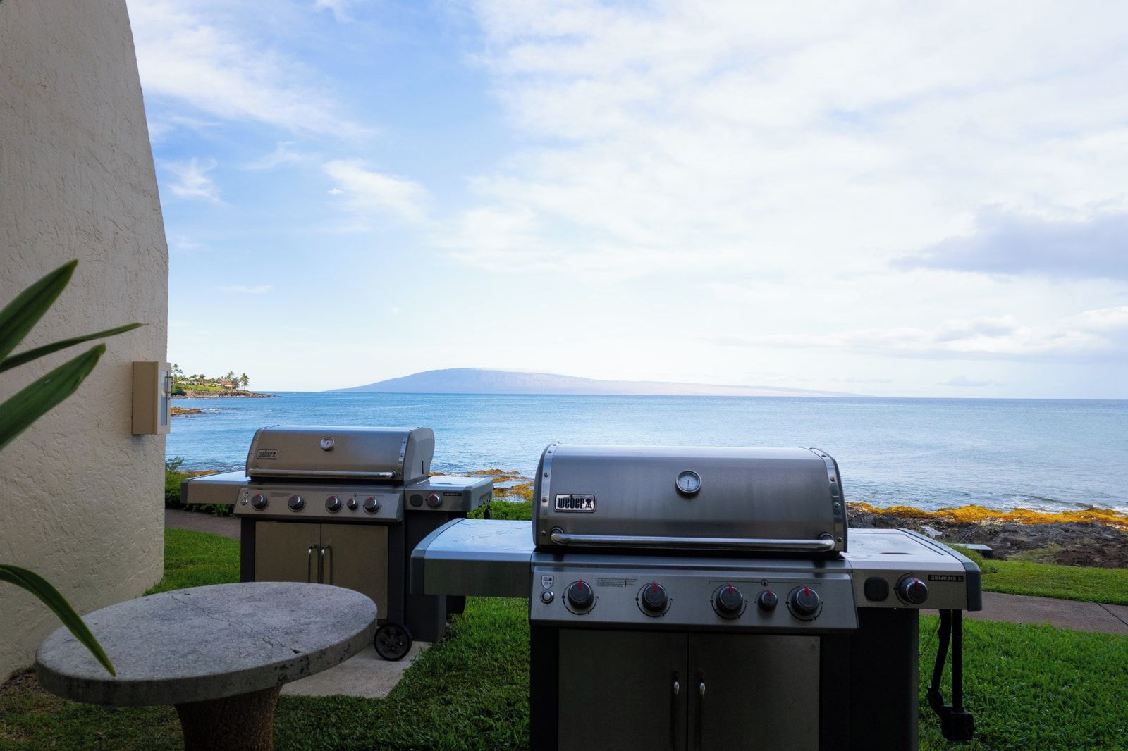 Two barbecue grills, a small round table, and a view of the ocean.