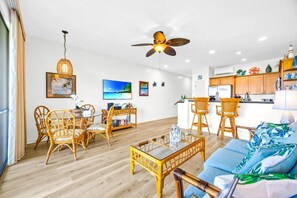 Ein modernes Wohnzimmer mit einem Glastisch, Korbstühlen, einem blauen Sofa und einem Deckenventilator.
