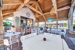 An outdoor seating area with white tables and chairs, a brick fireplace, and a wooden ceiling. - Golden Hour Seacrest by Stay on 30a (Seacrest Beach)