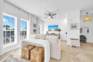 A modern living room with a white sofa, a ceiling fan, and a large window with a view of palm trees. - Golden Hour Seacrest by Stay on 30a (Seacrest Beach)