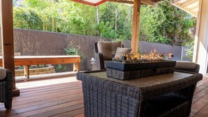 A covered outdoor patio with wicker furniture, a fire feature, and a wooden table. - The Rose House: Spacious Retreat w/ Fire Pit Deck/ near expo & Airport/Sleeps 8 (Central Point)