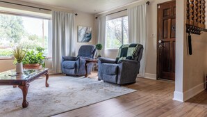 A living room with two armchairs, a coffee table, a potted plant, a painting on the wall, and a wooden door. - The Rose House: Spacious Retreat w/ Fire Pit Deck/ near expo & Airport/Sleeps 8 (Central Point)