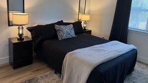 Ein ordentlich eingerichtetes Schlafzimmer mit Bett, zwei Nachttischen, einem Spiegel und einem Fenster mit Vorhängen.