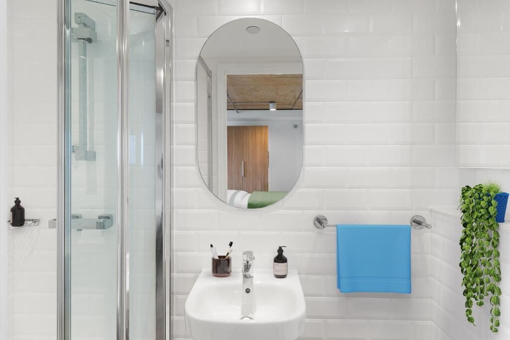 Een badkamer met een douchecabine van glas, een wit wastafelmeubel met een spiegel erboven en een blauwe handdoek aan de muur.