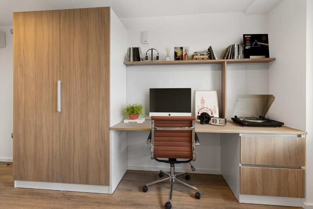 A modern office space with a wooden wardrobe, a desk with a computer, a chair, and shelves with books and decorative items.