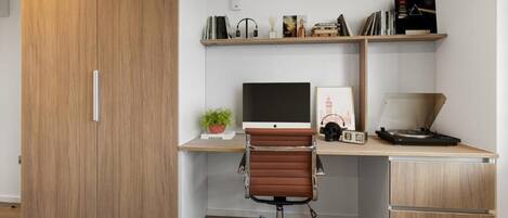Un espacio de oficina moderno con un armario de madera, un escritorio con computadora, una silla y estanterías con libros y objetos decorativos.
