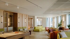 A modern hotel lobby with a pool table, green and orange sofas, and a large window providing natural light. - Canvas Wembley Arthur House (Wembley)