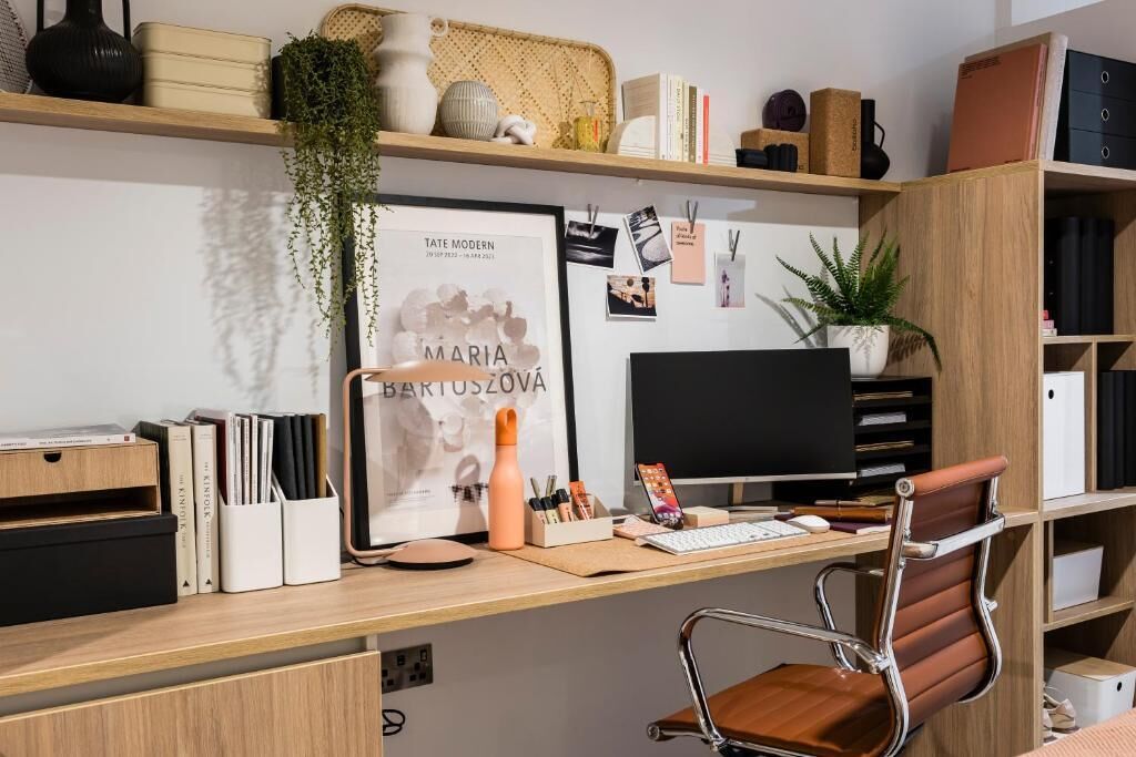 A modern office desk with a computer, keyboard, mouse, and various office supplies. There is a framed picture on the wall and a plant on the desk.