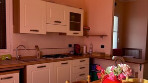 A kitchen with white cabinets, a sink, a stove, and a dining table with a red vase. - Casa Dunà - Mareri apartments (Costarainera)
