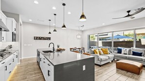 A modern kitchen with a central island, white cabinetry, and a dining area with a gray sofa and ottoman. - Luna Luxe Rooftop Retreat | 3BR • 2.5BA • Pool (Scottsdale)