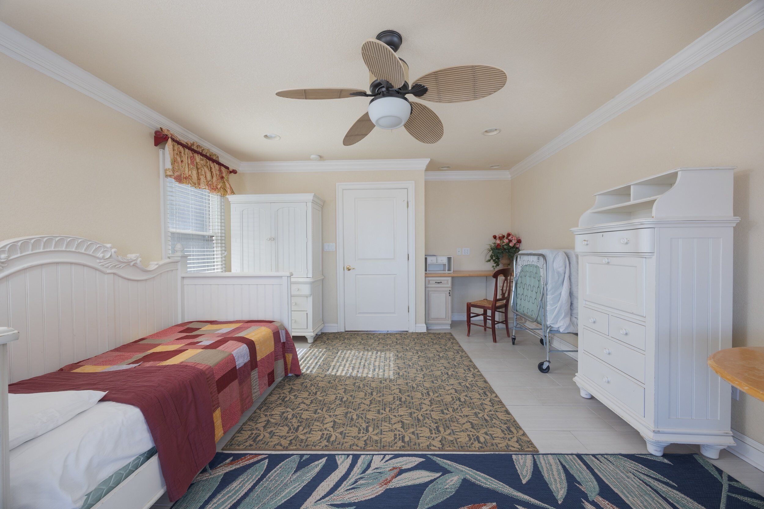 A bedroom with a bed, a desk, a chair, a wardrobe, and a ceiling fan.
