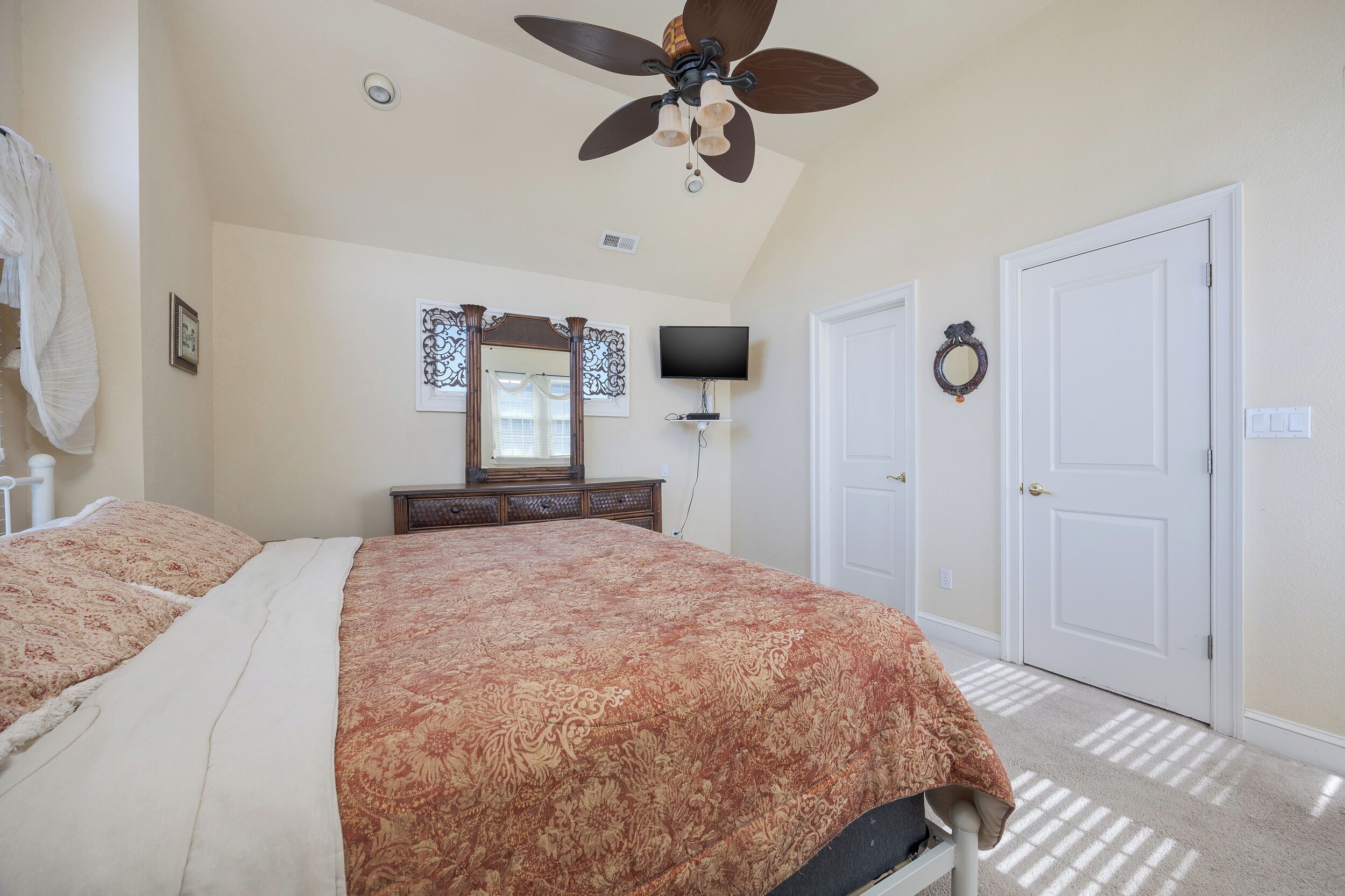 A bedroom with a large bed, a ceiling fan, a TV, and a door.